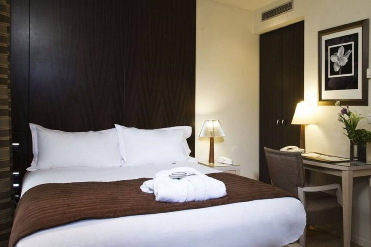 Une chambre d’hôtel avec un lit, un bureau, une chaise, une lampe, un téléphone et un tableau encadré au mur.