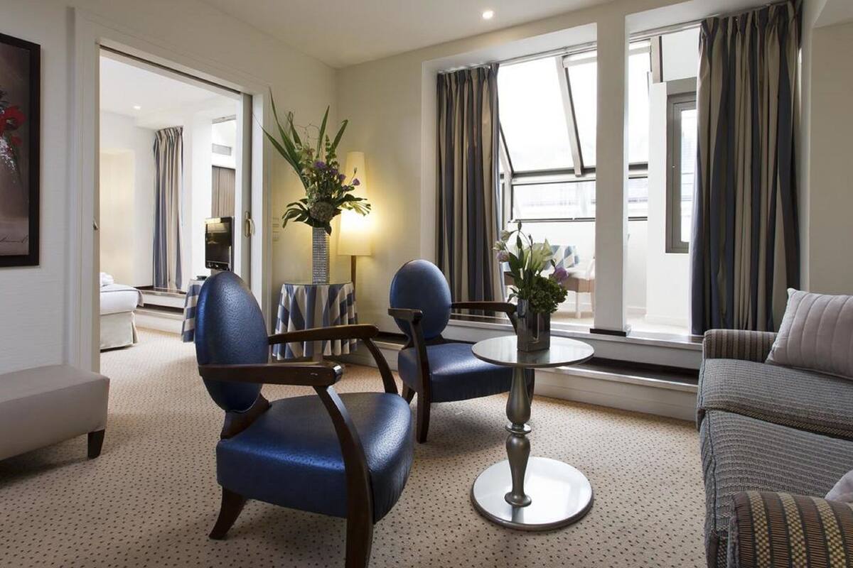 Une chambre d’hôtel moderne, équipée d’un canapé, de deux fauteuils, d’une petite table et d’une plante en pot.