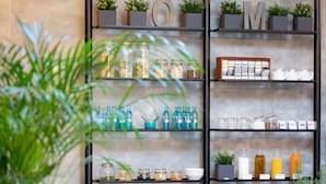 Un comedor moderno con una mesa larga, sillas negras y una unidad de estanterías fijada a la pared con plantas y utensilios de cocina.