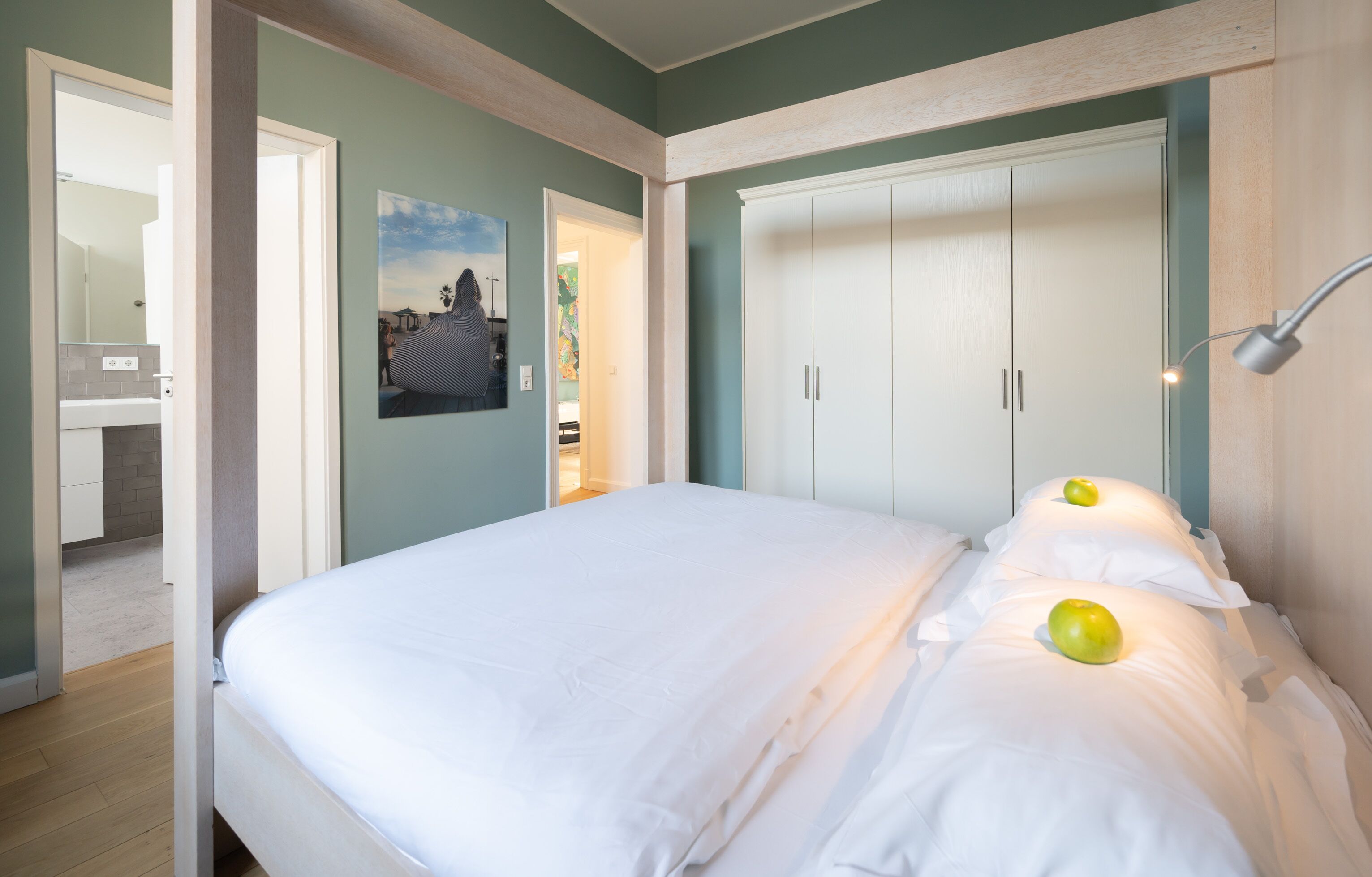 A bedroom with a bed, white walls, a wardrobe, and a painting.