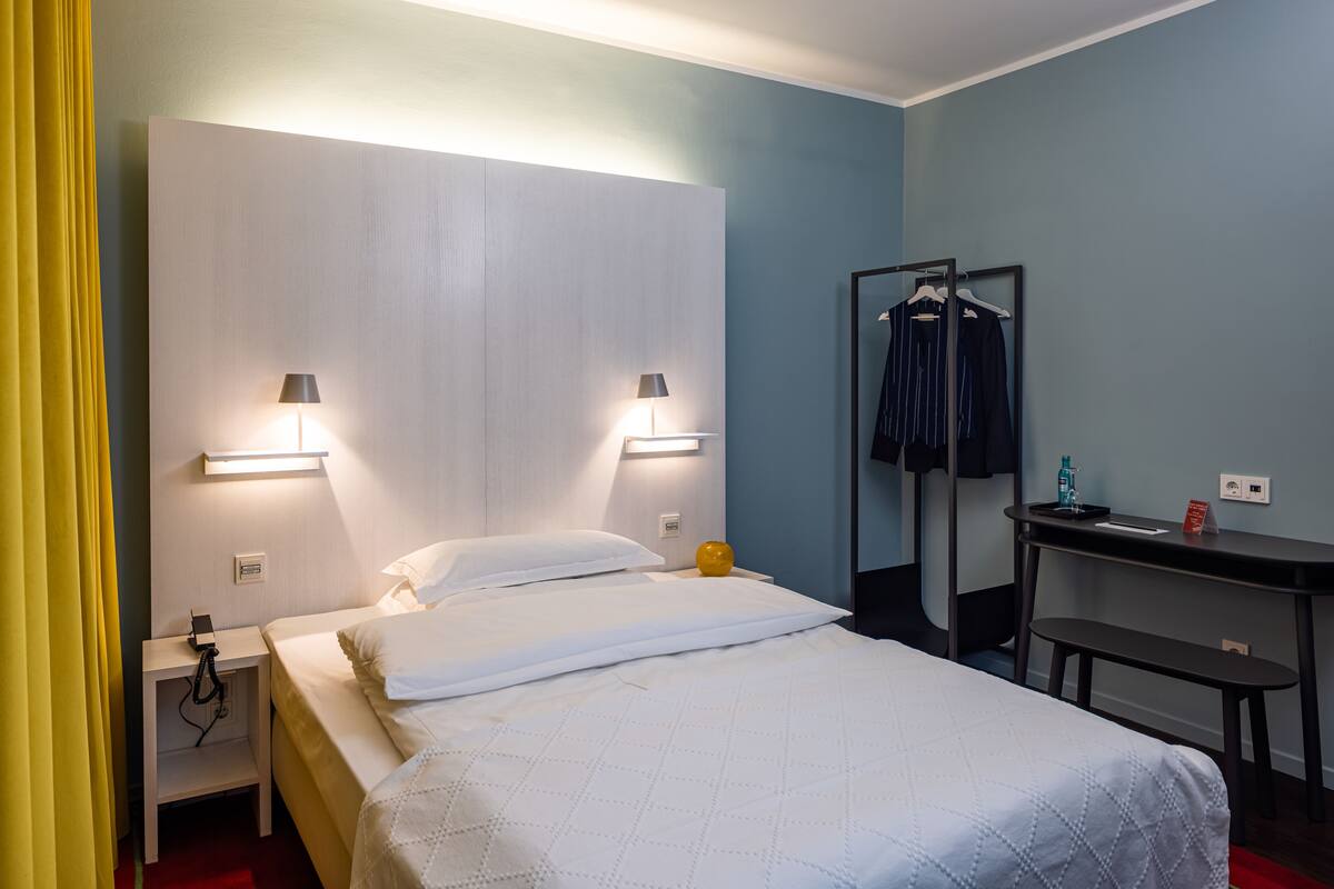 A hotel room with a bed, bedside lamps, a desk, and a mirror.