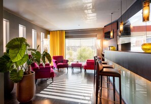 Experience the sleek lobby with a bar, seating areas, and a lush potted plant.