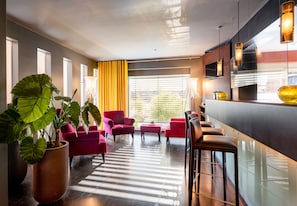 Experience the sleek lobby with a bar, seating areas, and a lush potted plant.