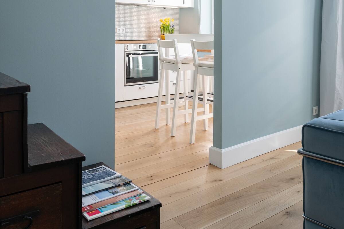 A modern kitchen with white cabinets, a dining area with a table and chairs, and a wooden floor.