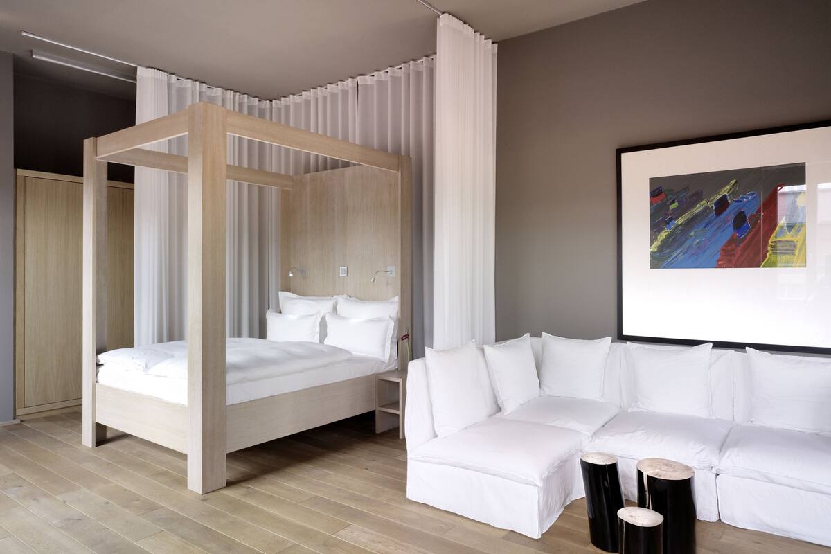 A modern bedroom with a canopy bed, a white sofa, and a painting on the wall.