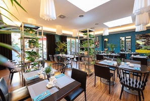 Enjoy dining in a stylish space with individual and communal seating, surrounded by lush greenery and natural light.