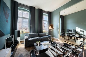 Ein modernes Wohnzimmer mit grauem Sofa, einem Couchtisch und einem Fernseher. Es gibt einen Essbereich mit Stühlen und einem Tisch.