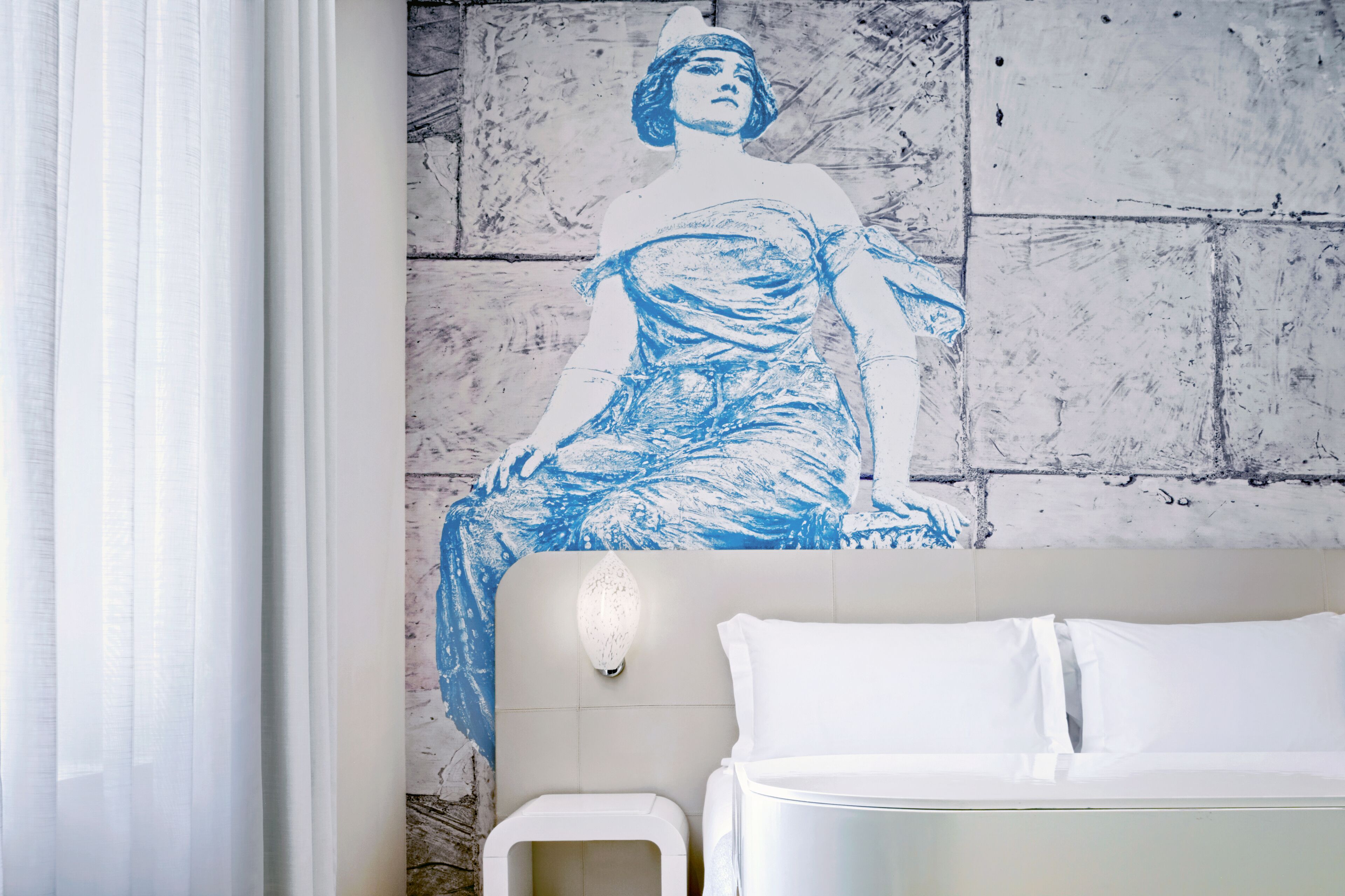 Una habitación de hotel con una cama, una lámpara de pared y un gran mural azul y blanco.