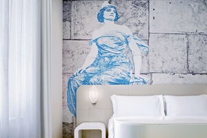 Una habitación de hotel con una cama, una lámpara de pared y un gran mural azul y blanco.