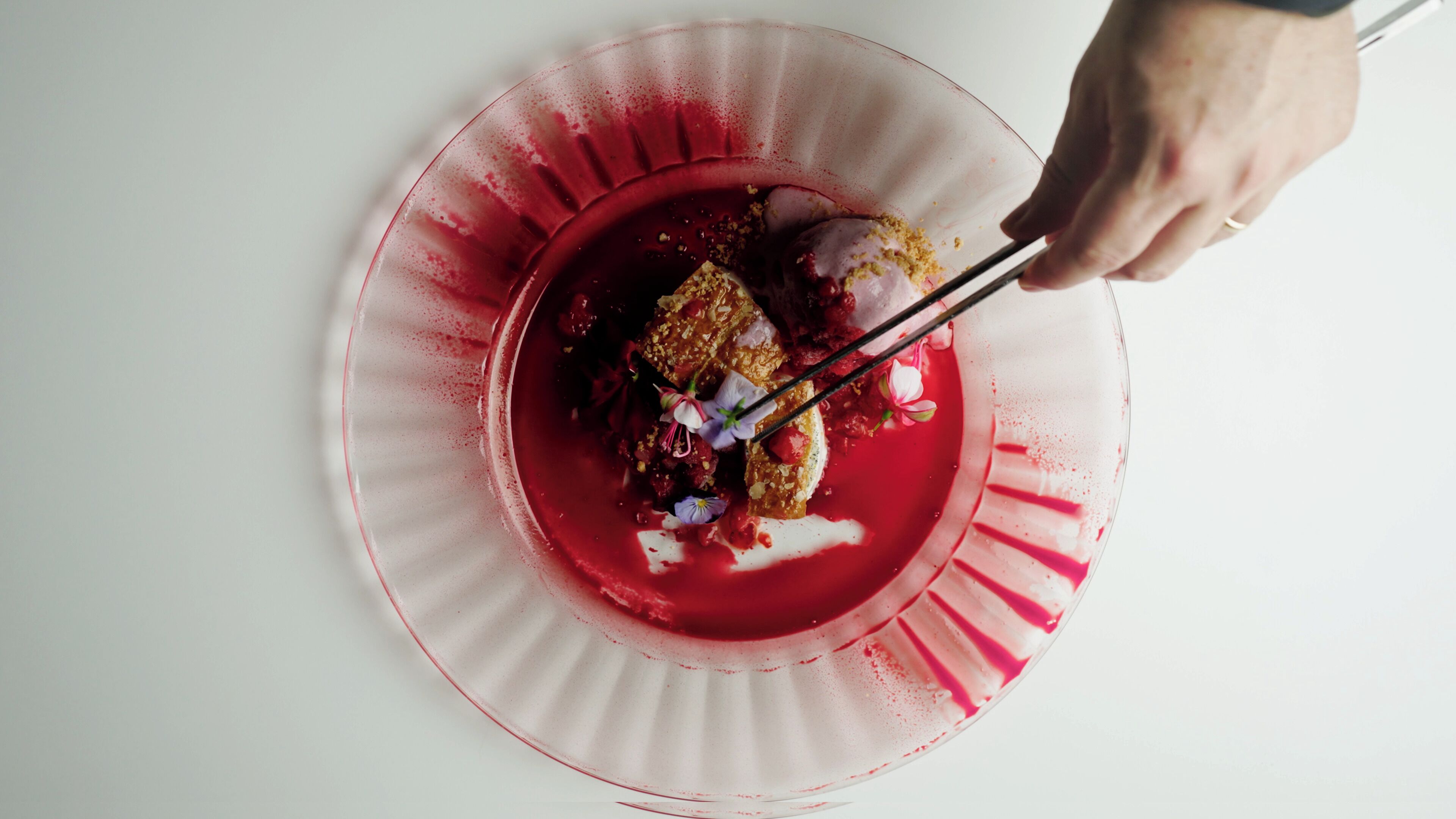 Een hand gebruikt stokjes om een dessert van een rood bord te pakken.