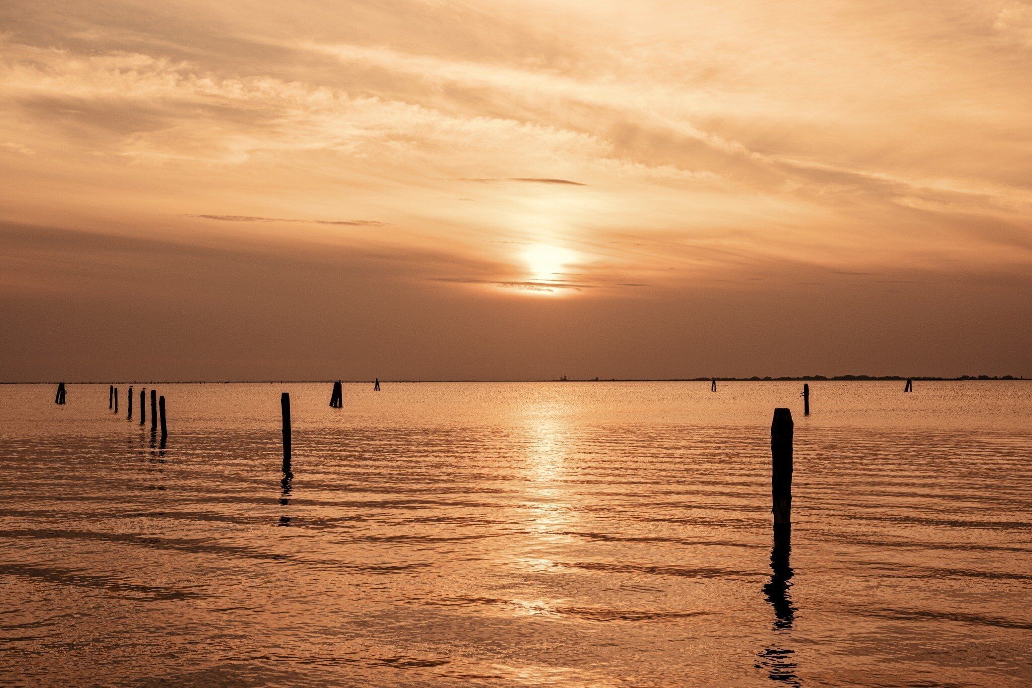 A sunset over a calm body of water with wooden posts in the foreground.