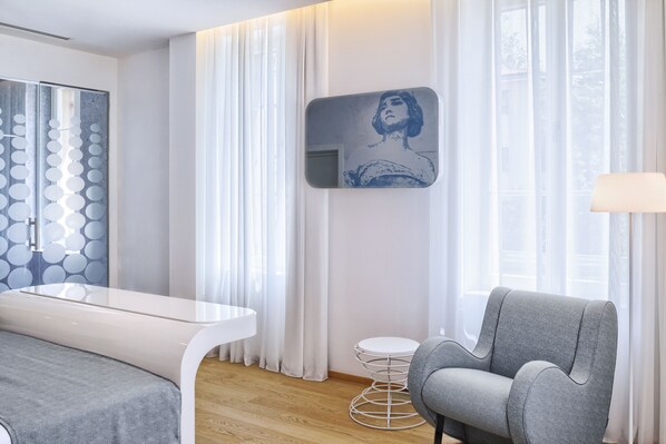 Una habitación moderna con un escritorio blanco, un sillón gris y una obra de arte colgada en la pared.