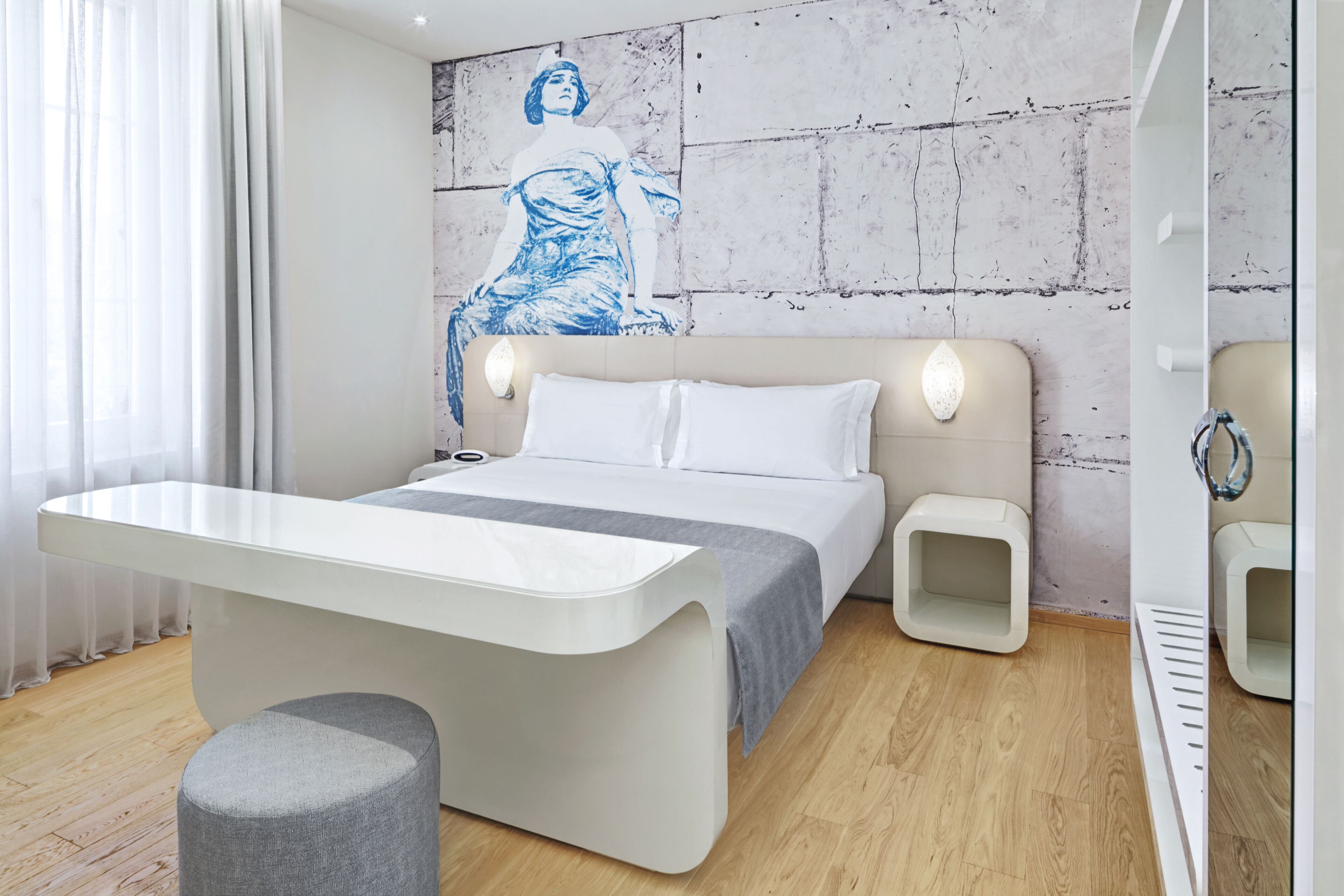Une chambre à coucher moderne, avec un lit, des tables de chevet, un bureau et une grande fenêtre agrémentée de rideaux légers.