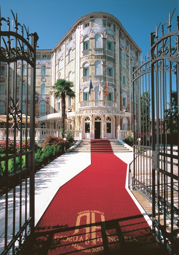 A grand hotel entrance with a red carpet leading to the doors, surrounded by ornate iron gates and a well-maintained garden. - Ausonia Hungaria (Venice)