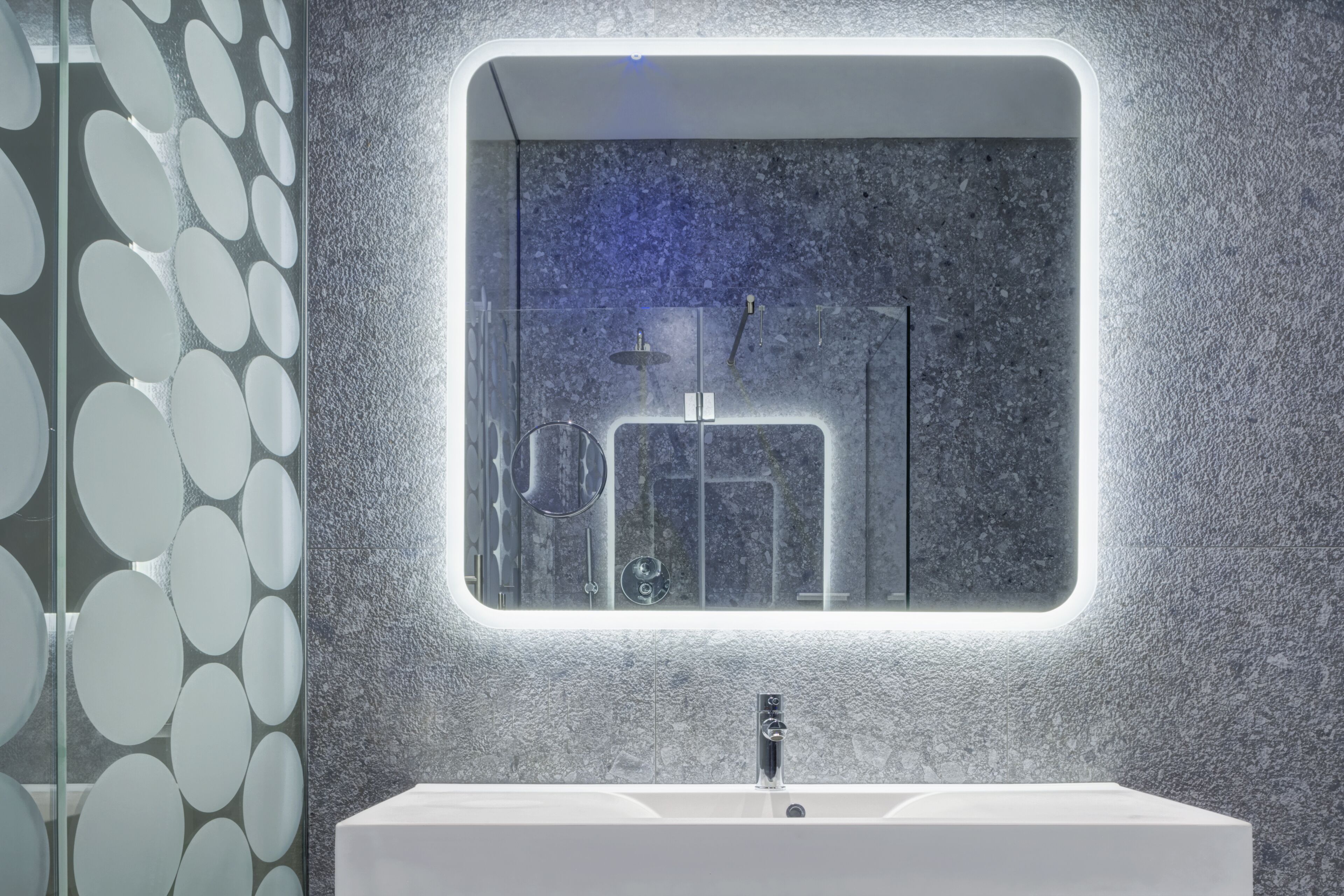 A modern bathroom with a large mirror, a white sink, and a textured wall.