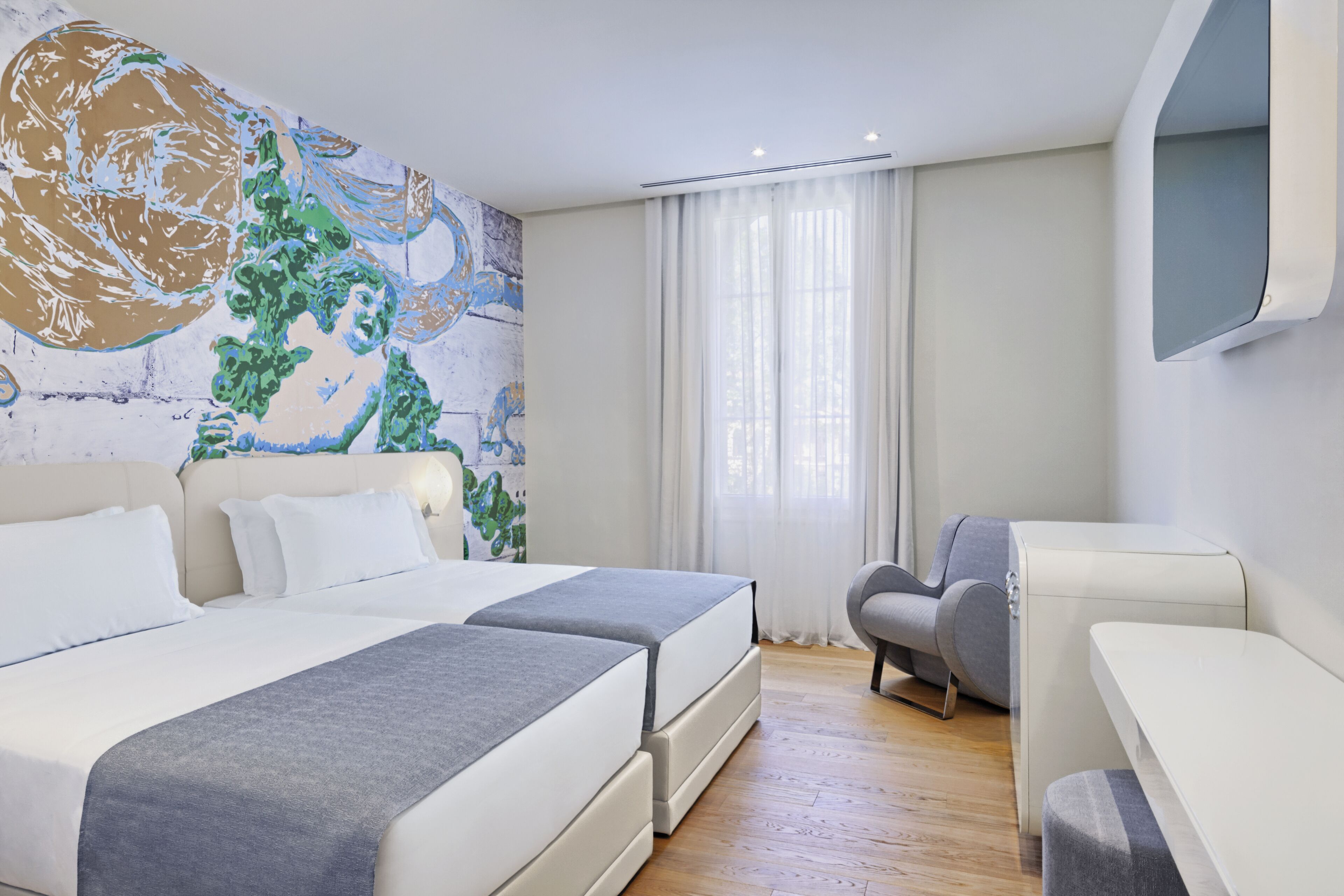 Una moderna camera d'albergo con due letti, un grande quadro astratto appeso al muro, una poltrona grigia e un piccolo tavolino.