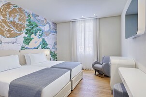 Una moderna camera d'albergo con due letti, un grande quadro astratto appeso al muro, una poltrona grigia e un piccolo tavolino.