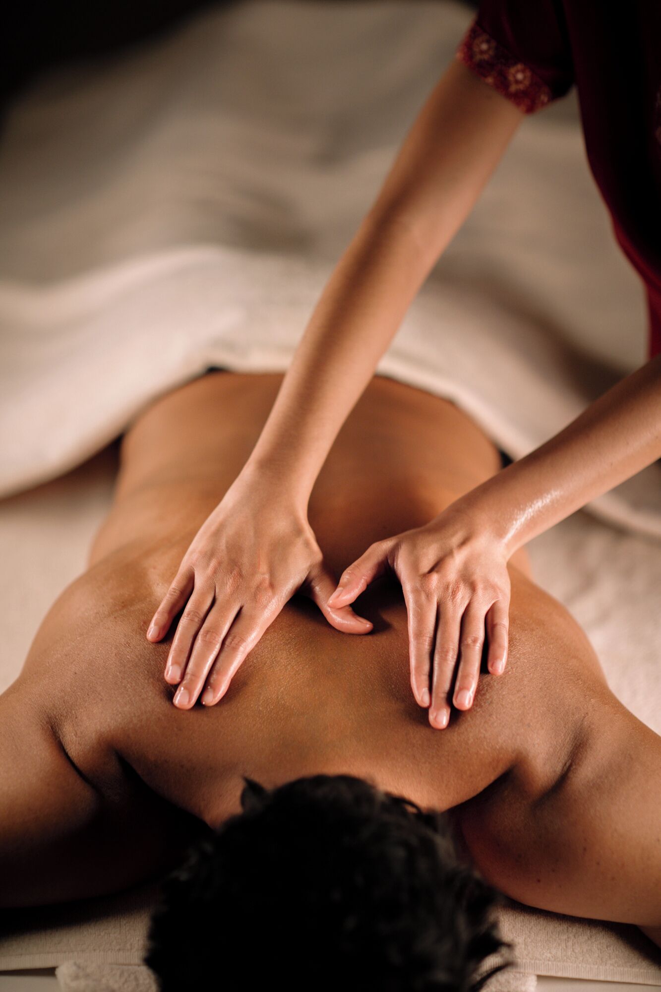 A massage therapy session with a person lying face down receiving hand massages on their back.