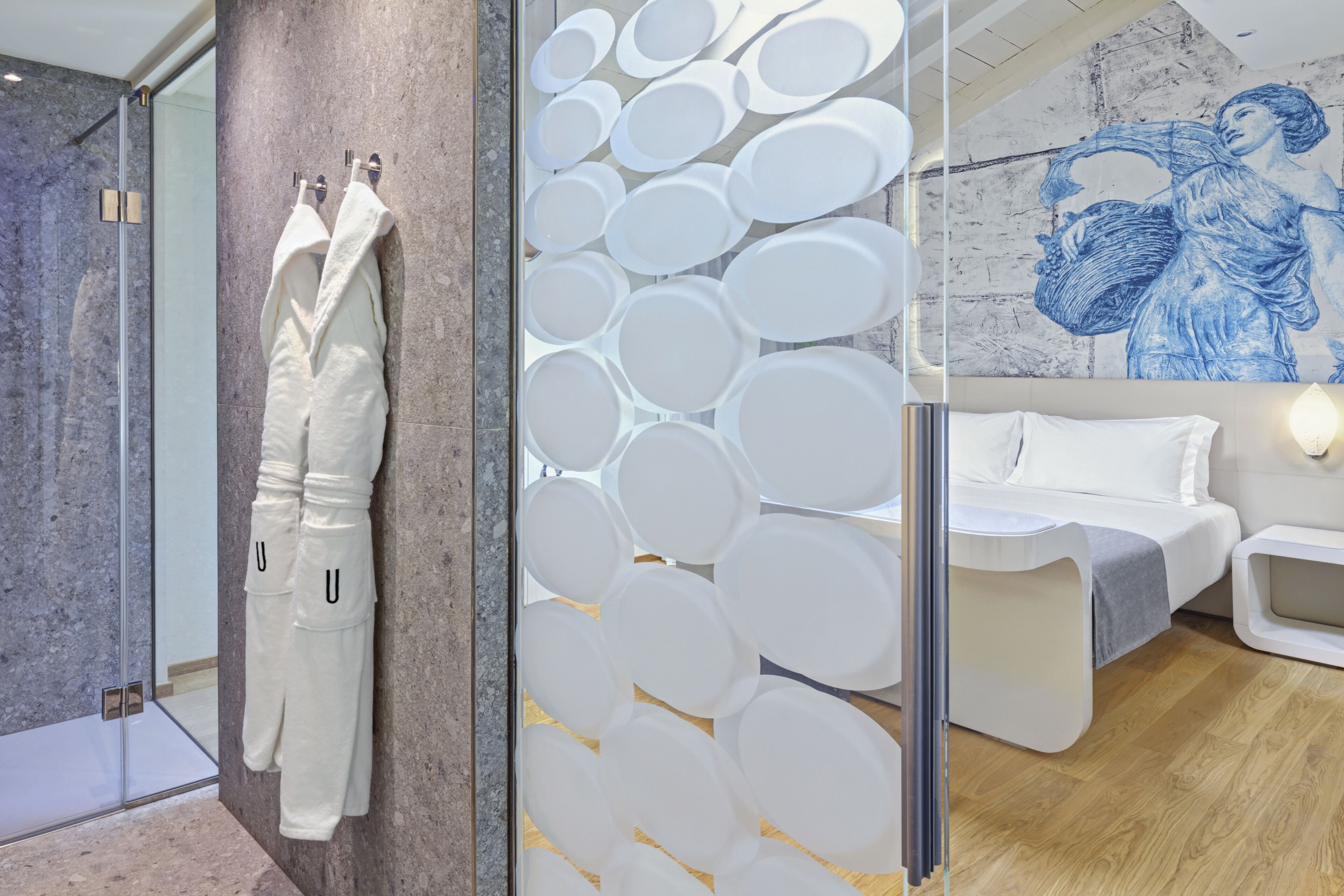 A modern hotel room with a glass shower, a bed with white bedding, and a wall with a circular pattern.