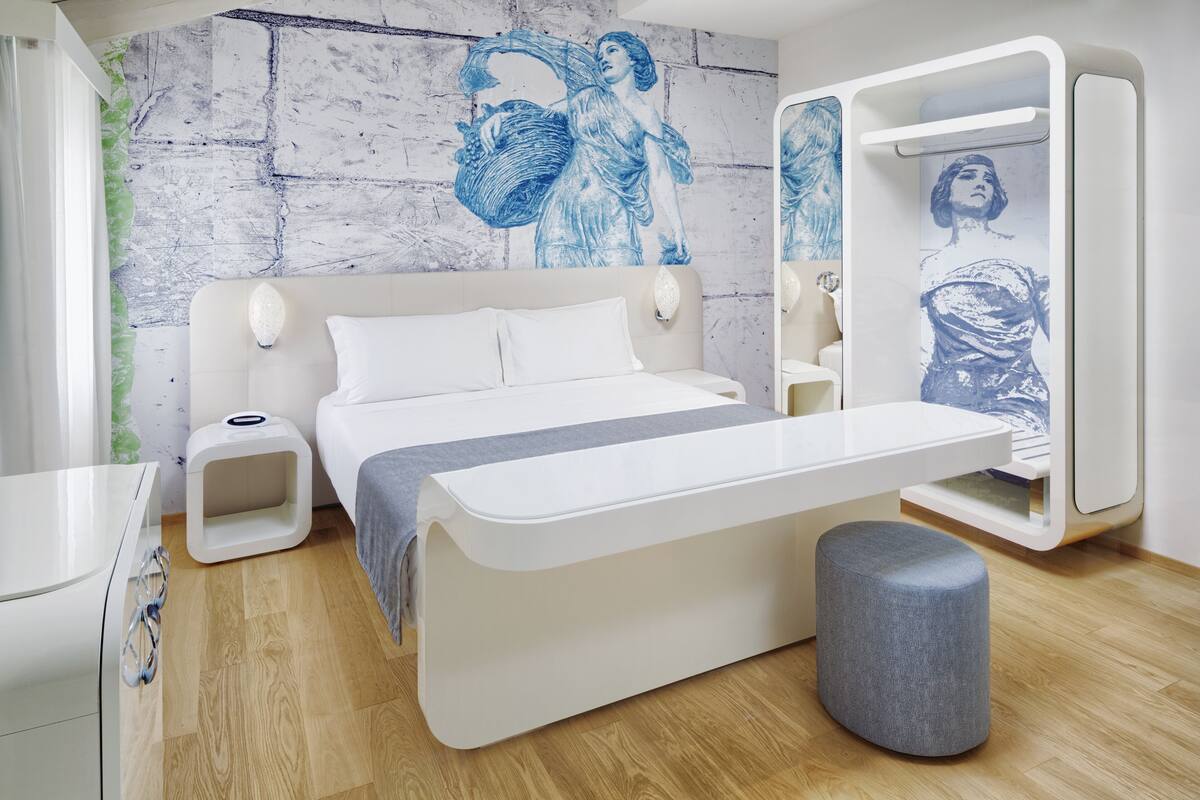 A modern bedroom with a bed, bedside tables, a bench, and a wall with artwork.