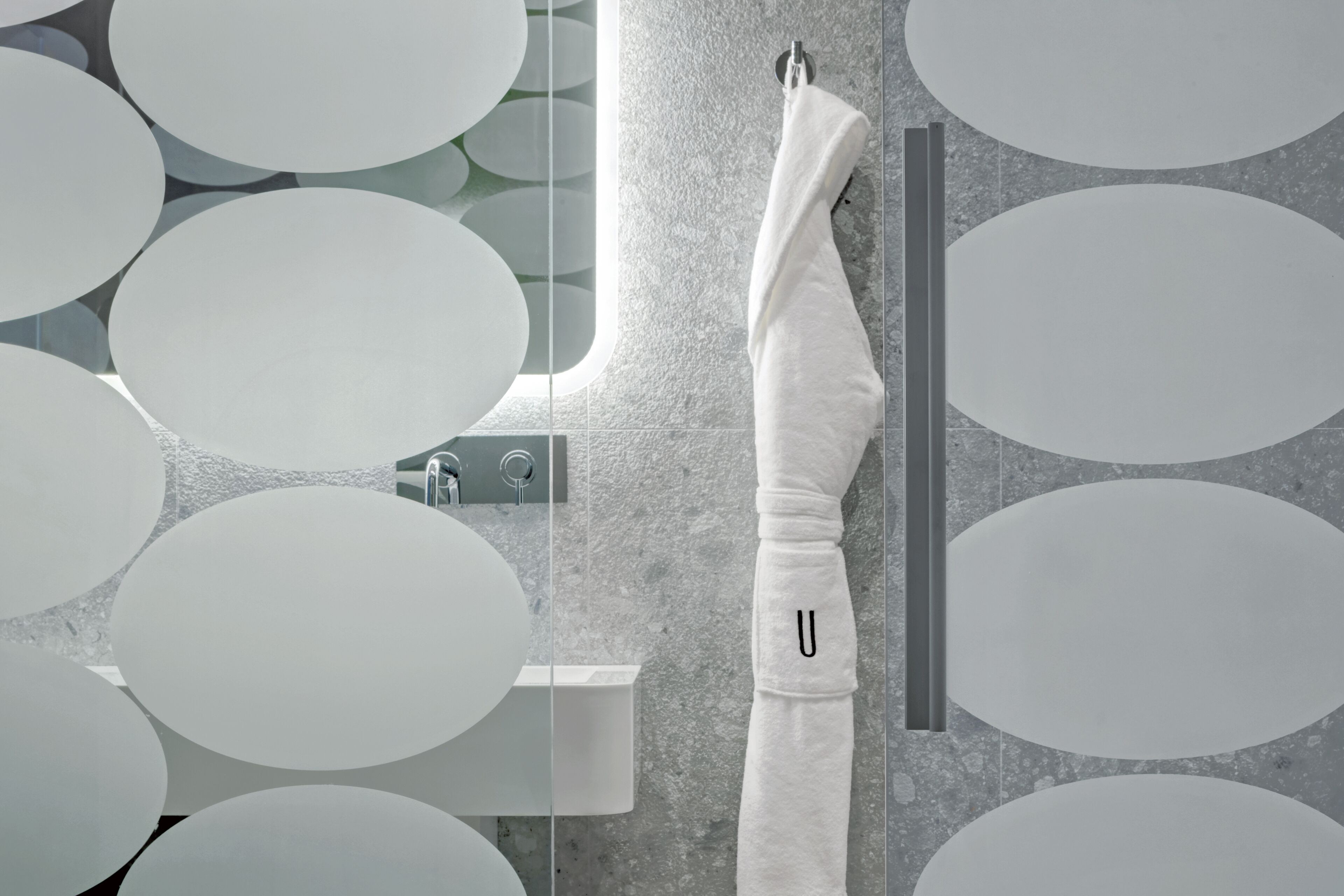 Une salle de bain équipée d’un porte-serviettes, d’un lavabo et d’un miroir orné de motifs circulaires sur le mur.