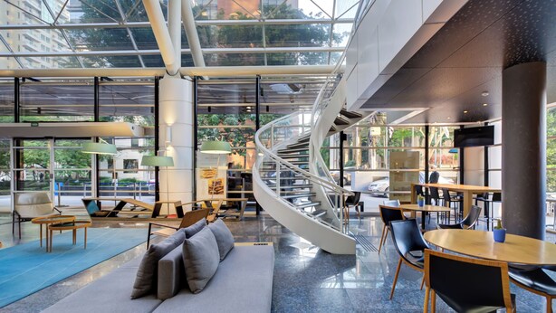 Un intérieur moderne agrémenté d’un escalier en colimaçon, de coins salon et de grandes fenêtres offrant une vue sur l’extérieur.