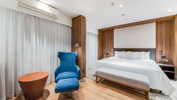 Een moderne hotelkamer met een groot bed, een blauwe fauteuil, een klein houten tafeltje en een nachtkastje met een lamp.