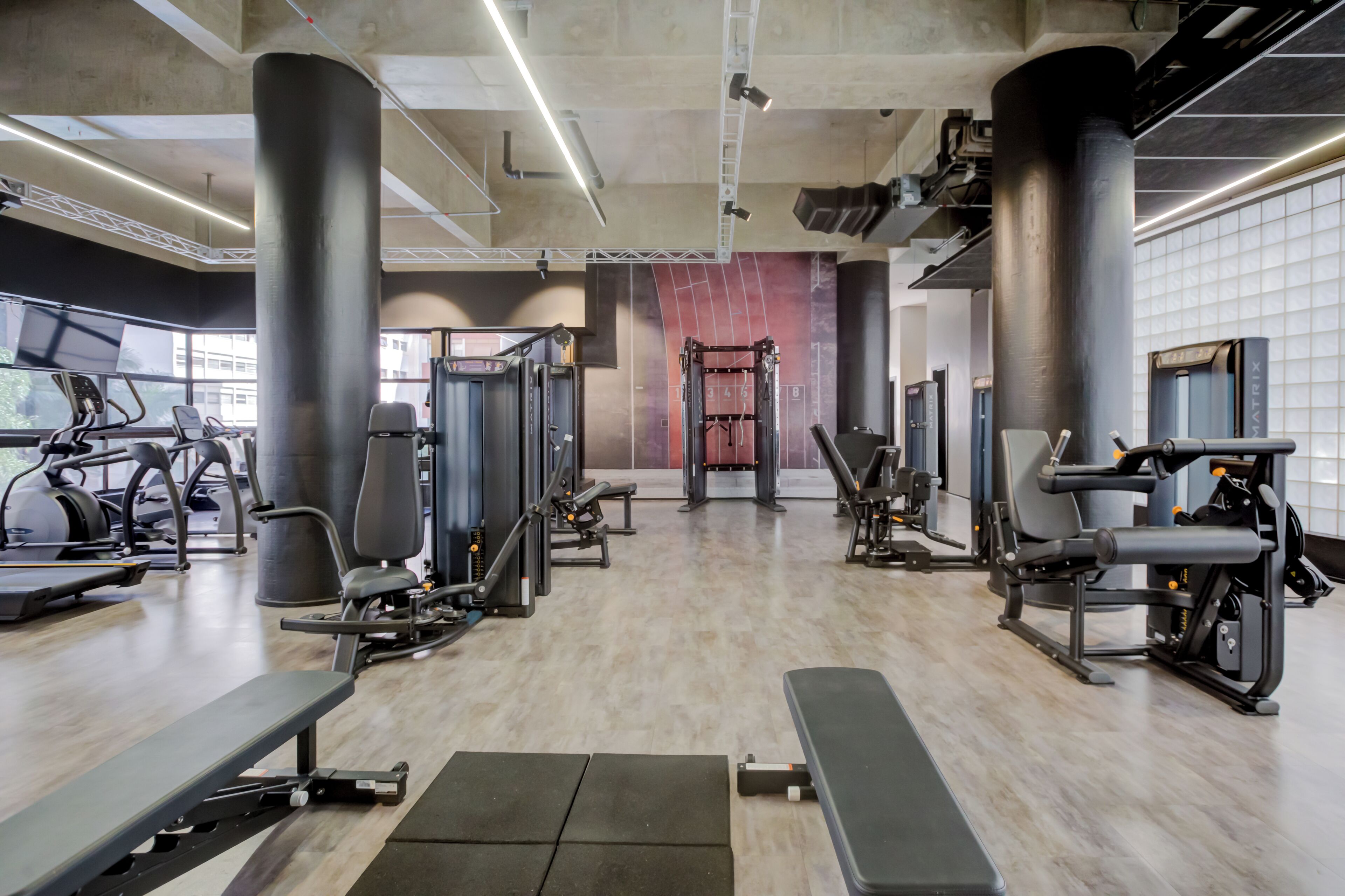 A gym with various exercise equipment, large windows, and a high ceiling.