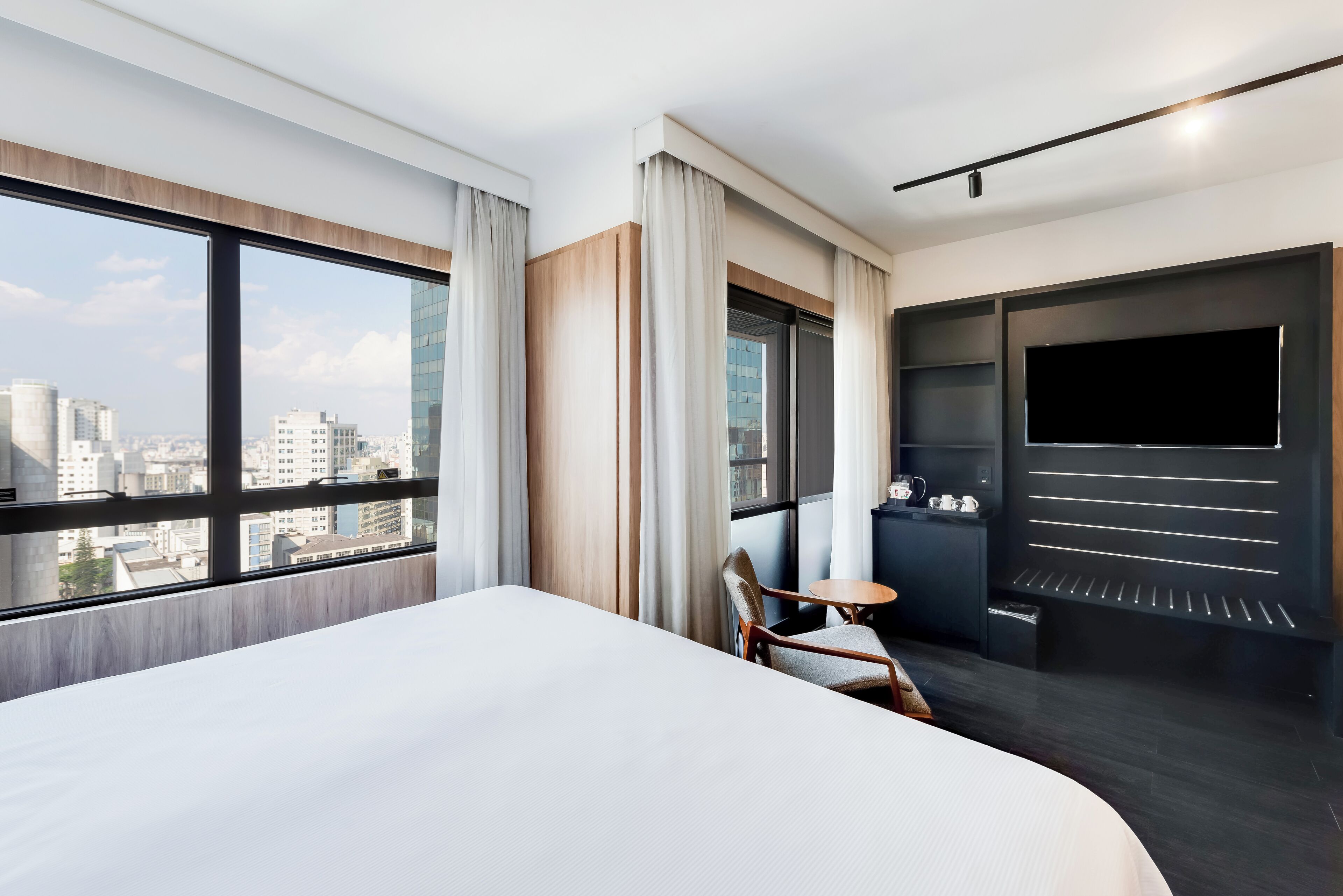 A modern hotel room with a large bed, a TV, a small table, and a chair.