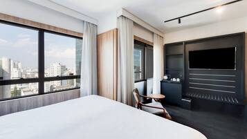 A modern hotel room with a large bed, a TV, a small table, and a chair.