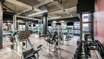 A spacious gym with various exercise equipment, large windows, and a high ceiling.