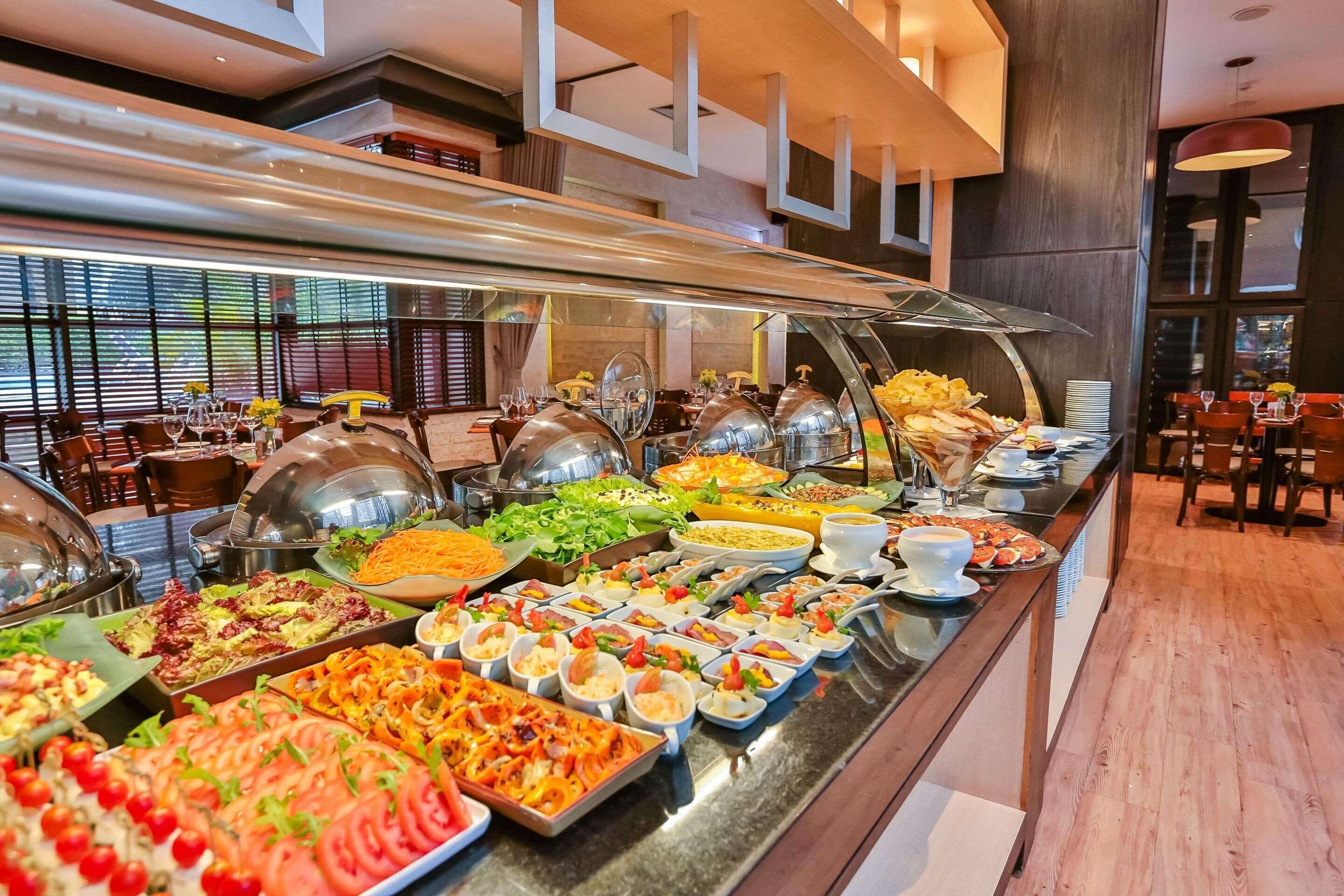 Buffet com diversos alimentos e área de refeições com mesas e cadeiras.