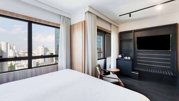 Quarto de hotel com uma cama grande, televisão, uma mesinha e uma cadeira.