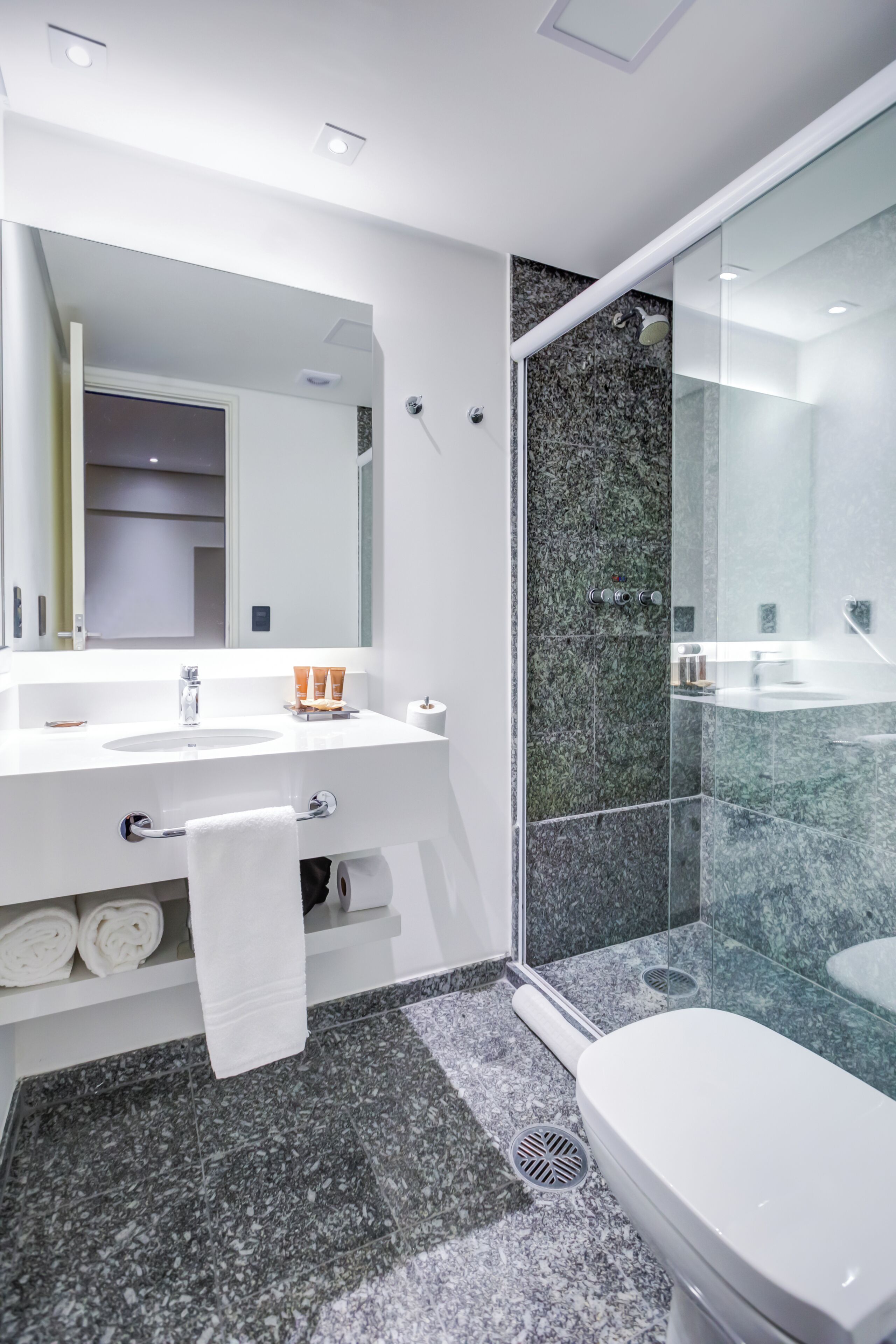 Un baño moderno con un tocador blanco, una mampara de ducha de vidrio y piso de baldosas de mármol.