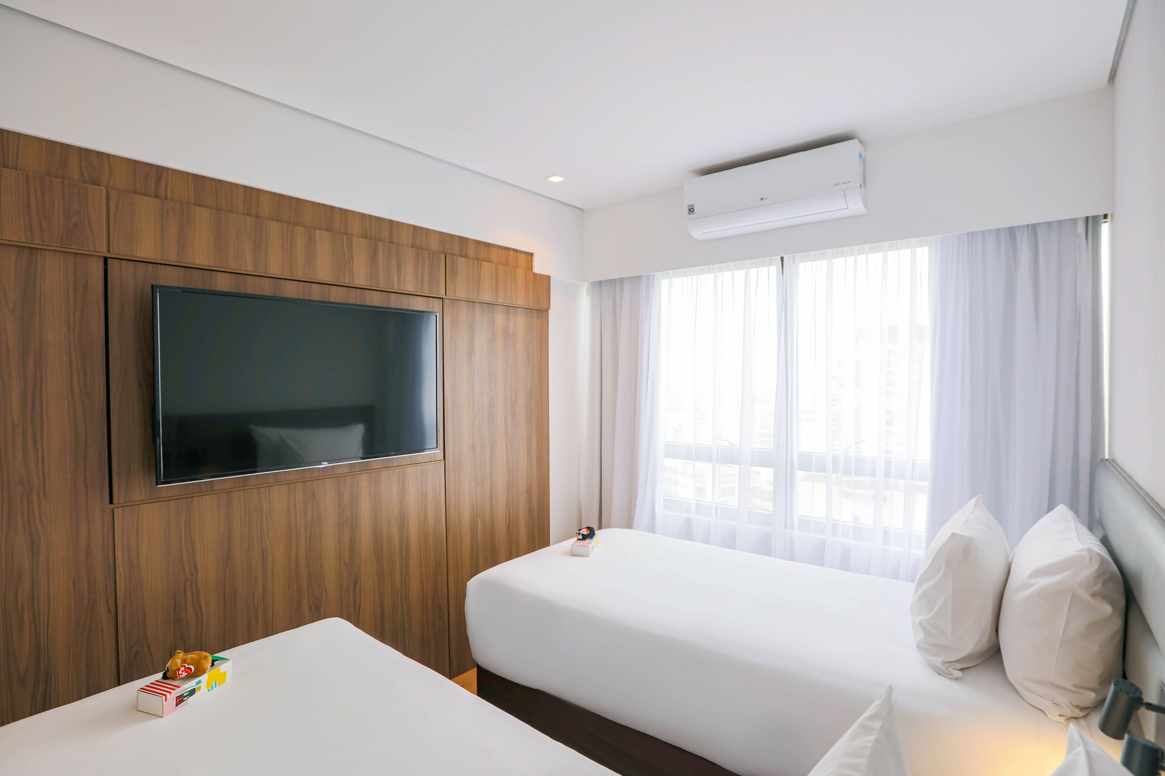 Quarto de hotel com duas camas, uma televisão fixada na parede e um ar condicionado.