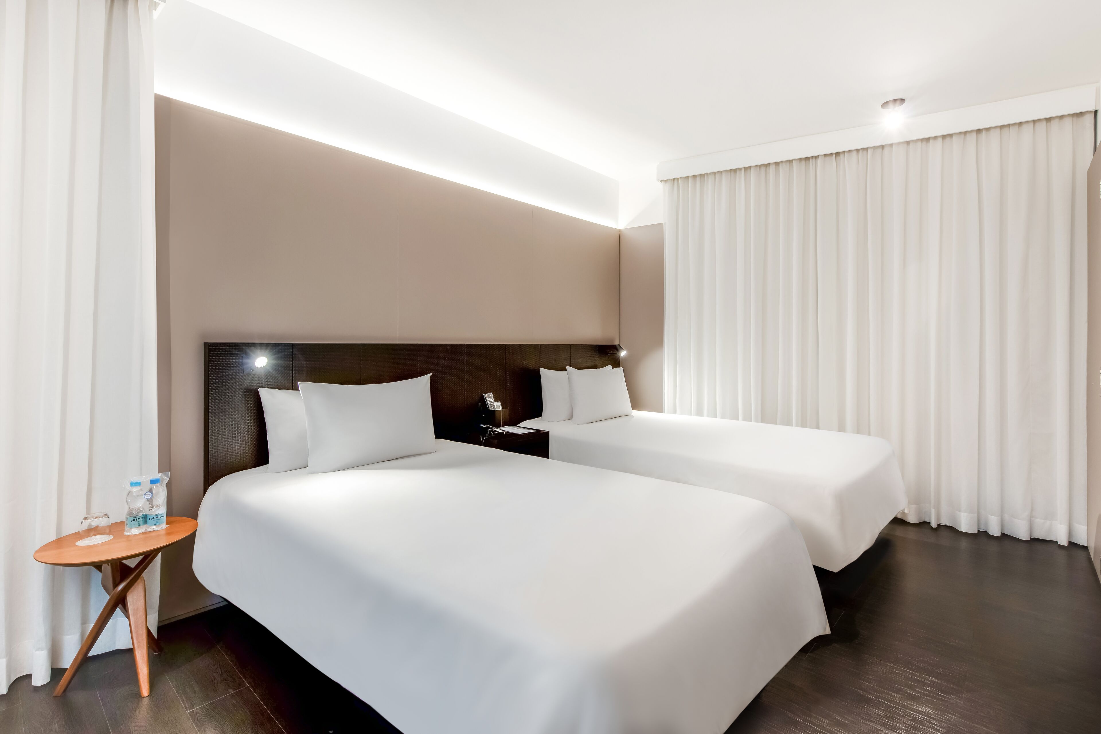 A hotel room with two beds, a small table with water bottles, a nightstand, and a headboard.