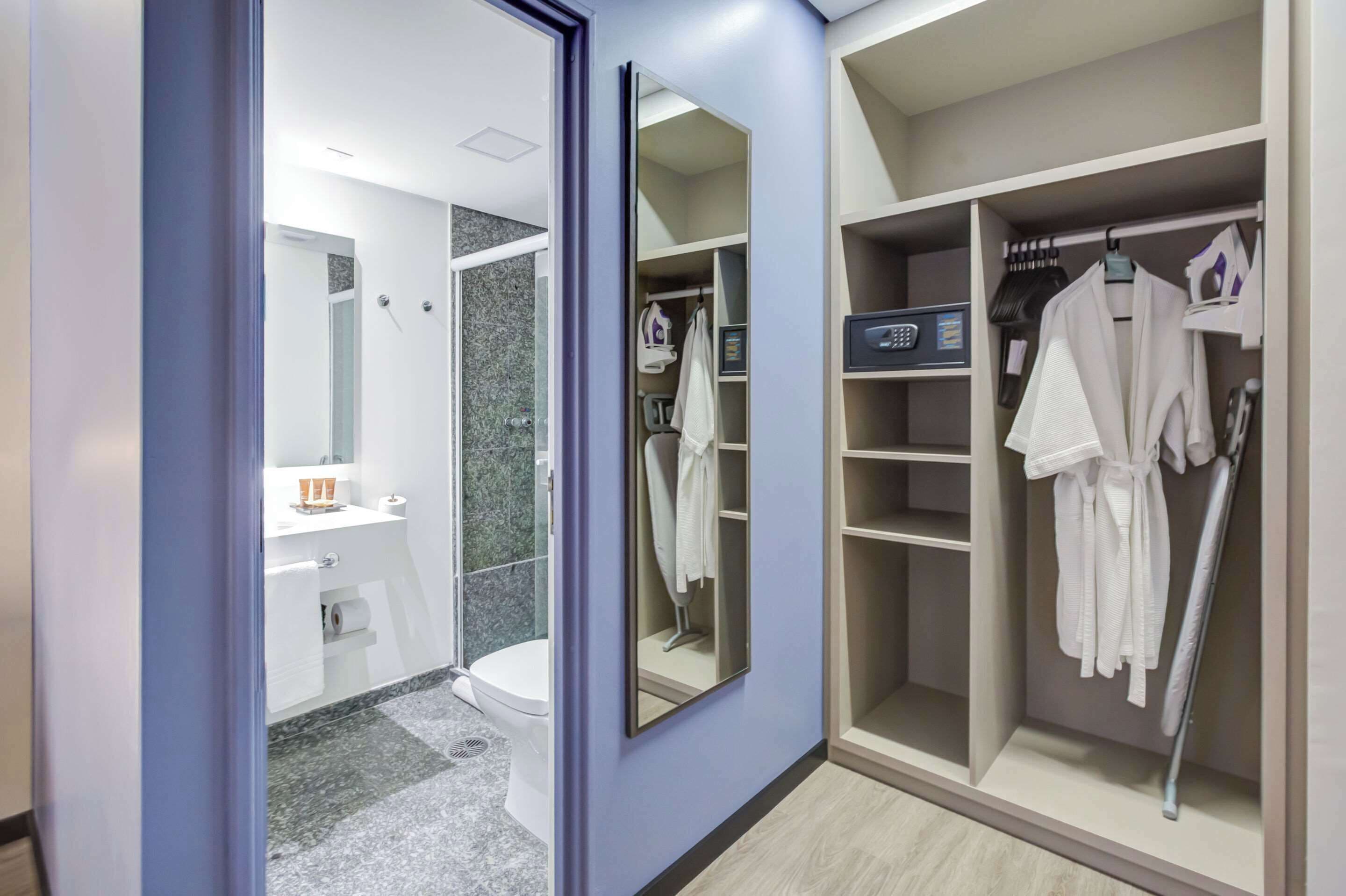 Un baño moderno con lavamanos, inodoro y ducha. Junto a él, un vestidor con repisas y ropa colgada.
