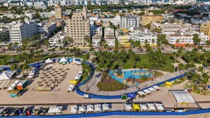 A coastal cityscape with a beachfront area featuring tents, a swimming pool, and a parking lot. - Hotel Ocean (Miami Beach)