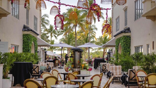 An outdoor patio with wicker chairs and tables, surrounded by lush greenery and palm trees. - Hotel Ocean (Miami Beach)