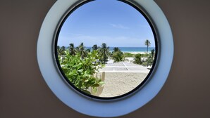 A circular window with a view of a beach, palm trees, and a clear sky. - Hotel Ocean (Miami Beach)
