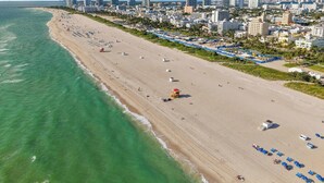 A coastal cityscape with a long sandy beach, a lifeguard tower, and a dense cluster of high-rise buildings in the background. - Hotel Ocean (Miami Beach)