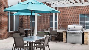 An outdoor patio with a brick building, a grill, and tables with chairs.