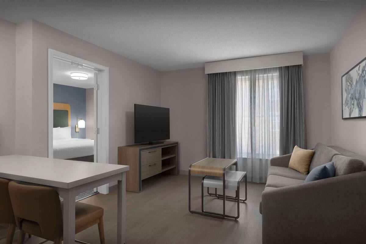 A modern hotel room with a bed, a TV, a dining table, and a sofa.