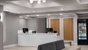 A modern hotel lobby with a reception desk, seating area, and a beverage refrigerator.