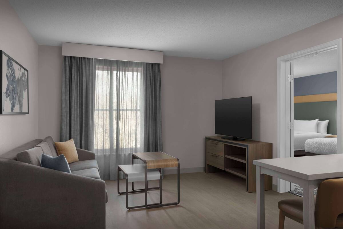 A modern hotel room with a sofa, a small table, a TV, and a bed.