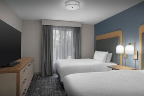 A hotel room with two beds, a TV, a desk, and a large mirror.