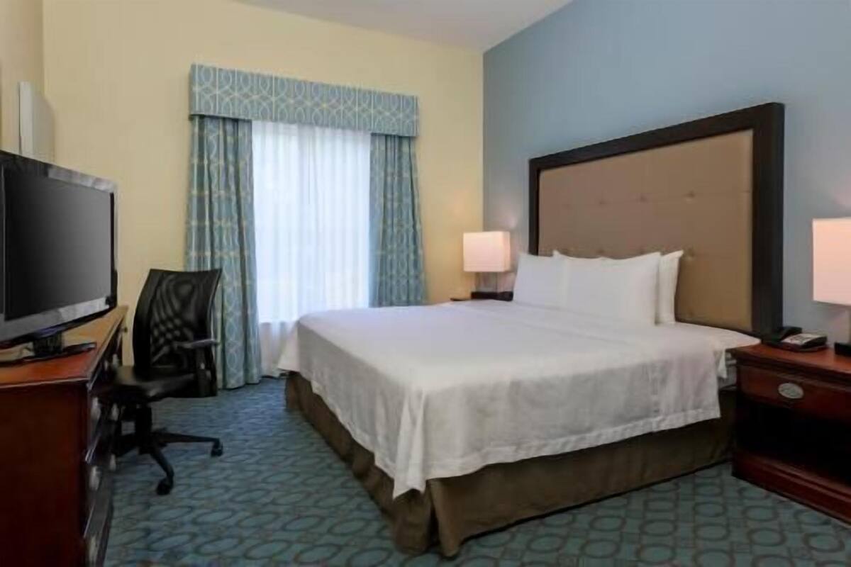 A hotel room with a bed, two bedside lamps, a television, and a desk with a chair.