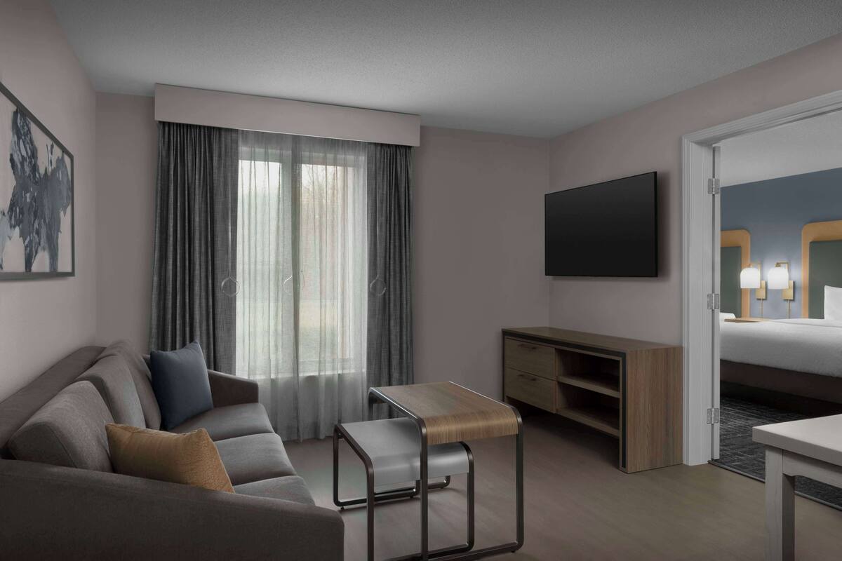 A modern hotel room with a sofa, a small table, a TV, and a bed.