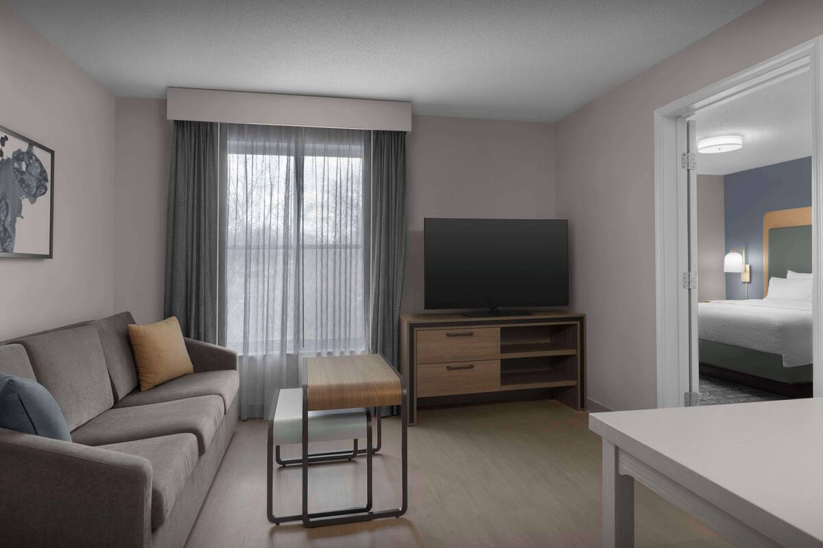 A modern hotel room with a sofa, a small table, a TV, and a bed.