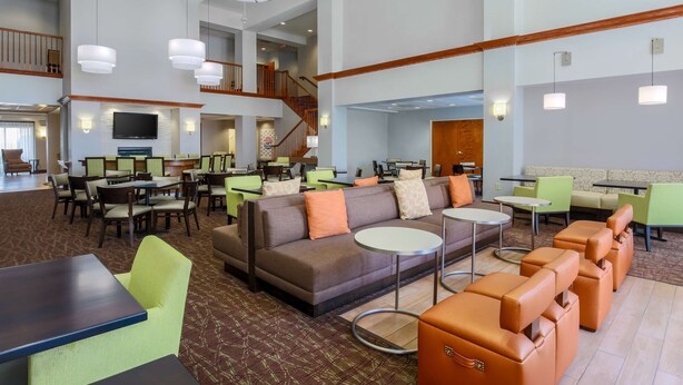 A spacious lobby with multiple seating areas, including sofas, chairs, and tables. There is a staircase leading to an upper level, and a flat-screen TV mounted on the wall. - Homewood Suites by Hilton Ft. Worth-North at Fossil Creek (Fort Worth)